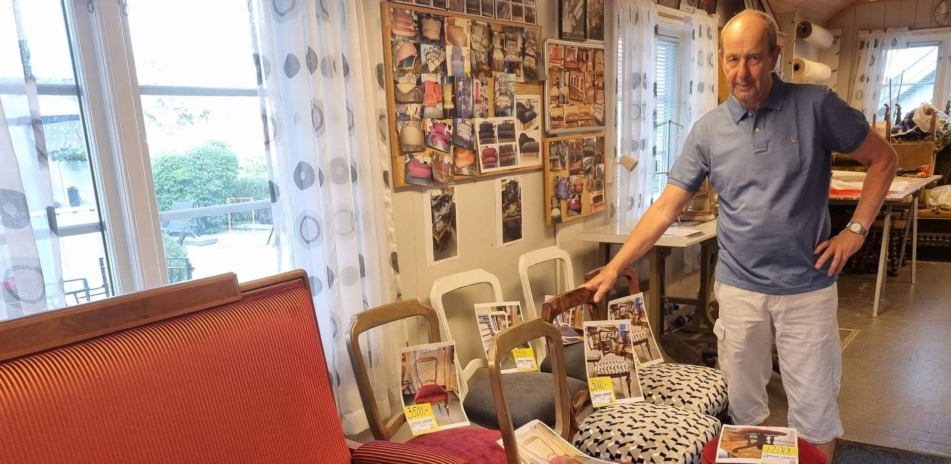 Birger Andresen står i verkstedet ved stoler med nye trekk og en rød sofa