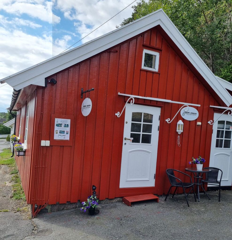 Bua, et lite rødt trehus med hvit dør og skilt på veggen